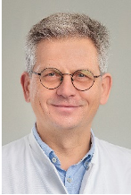 Porträt eines älteren Mannes mit grauen Haaren und weißem Hemd vor hellem Hintergrund